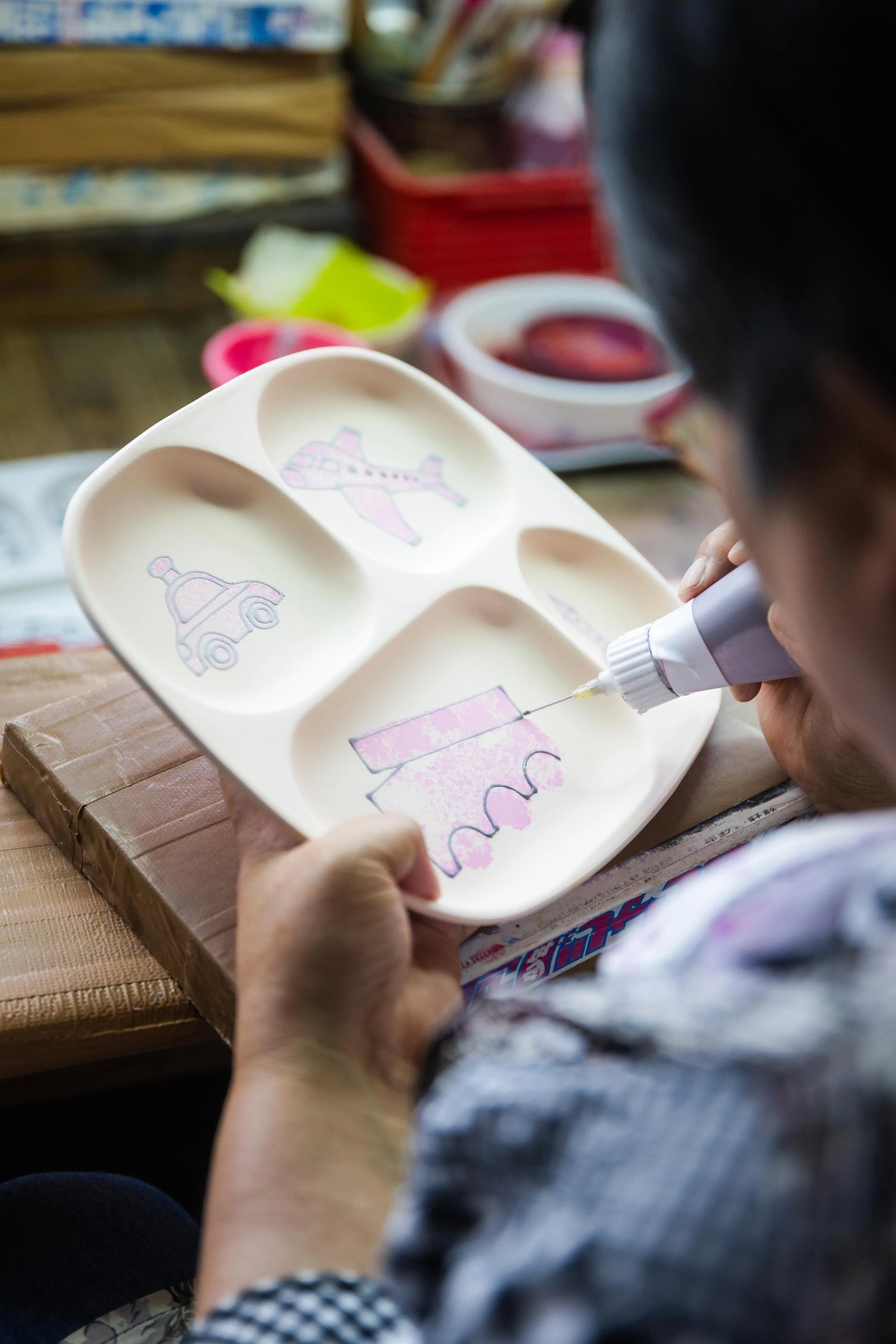 Japanese ceramic kids divided plate being hand decorated with playful vehicle motifs by an artisan at Oishin Kiln in Japan