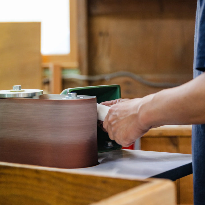 Craftsperson shaping a wooden piece on a rotating sander in a Japanese workshop