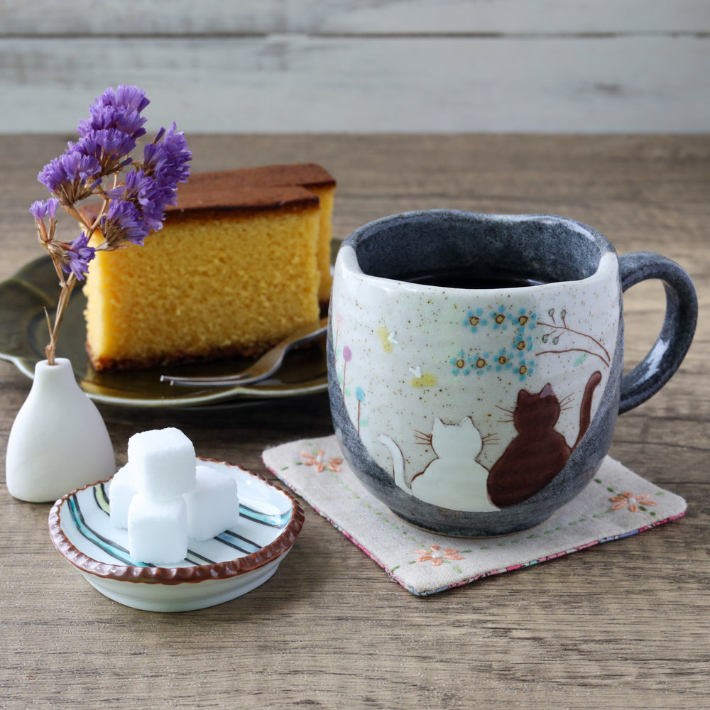 Handcrafted ceramic mug with two illustrated cats, served with black coffee, sugar cubes, and castella cake.