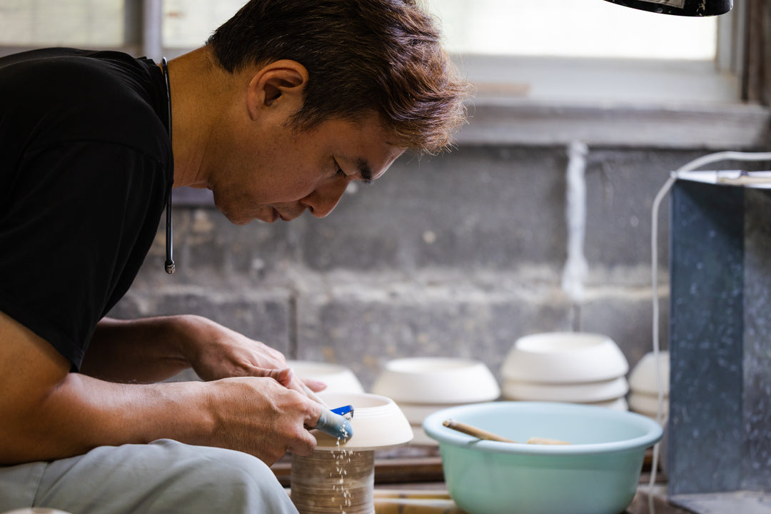Japanese artisan carefully carving intricate grooves into a white ceramic piece on a pottery wheel at Riso Kiln
