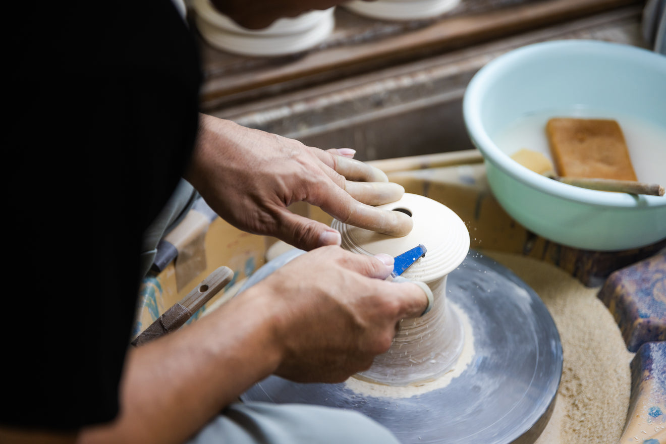 Close up of a Japanese artisan hand carving fine lines on a white ceramic piece on a pottery wheel at Riso Kiln