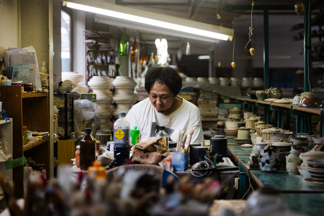 Japanese ceramic artist hand painting intricate details on pottery inside Rizaemon Kiln studio in Nagasaki Japan