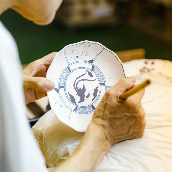 Hand painting traditional patterns on an unglazed Japanese porcelain plate at a kiln workshop.