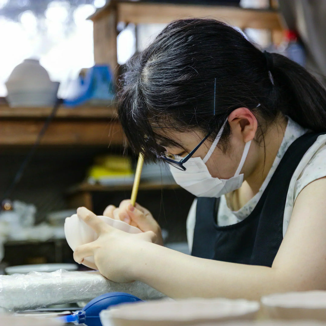 Artisan painting fine details on a scalloped ceramic bowl at a Japanese kiln workspace