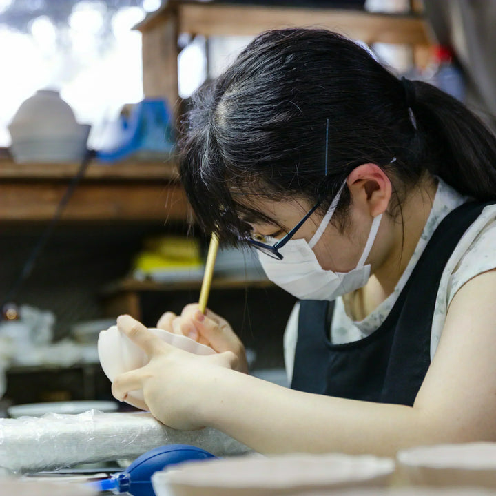 Artisan painting fine details on a scalloped ceramic bowl at a Japanese kiln workspace