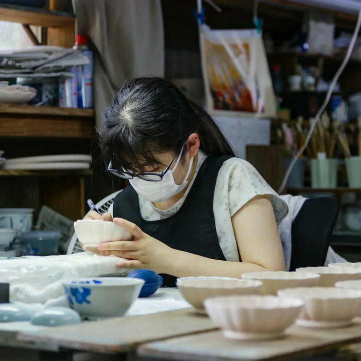 Craftsperson hand painting scalloped ceramic bowls in a traditional Japanese pottery studio