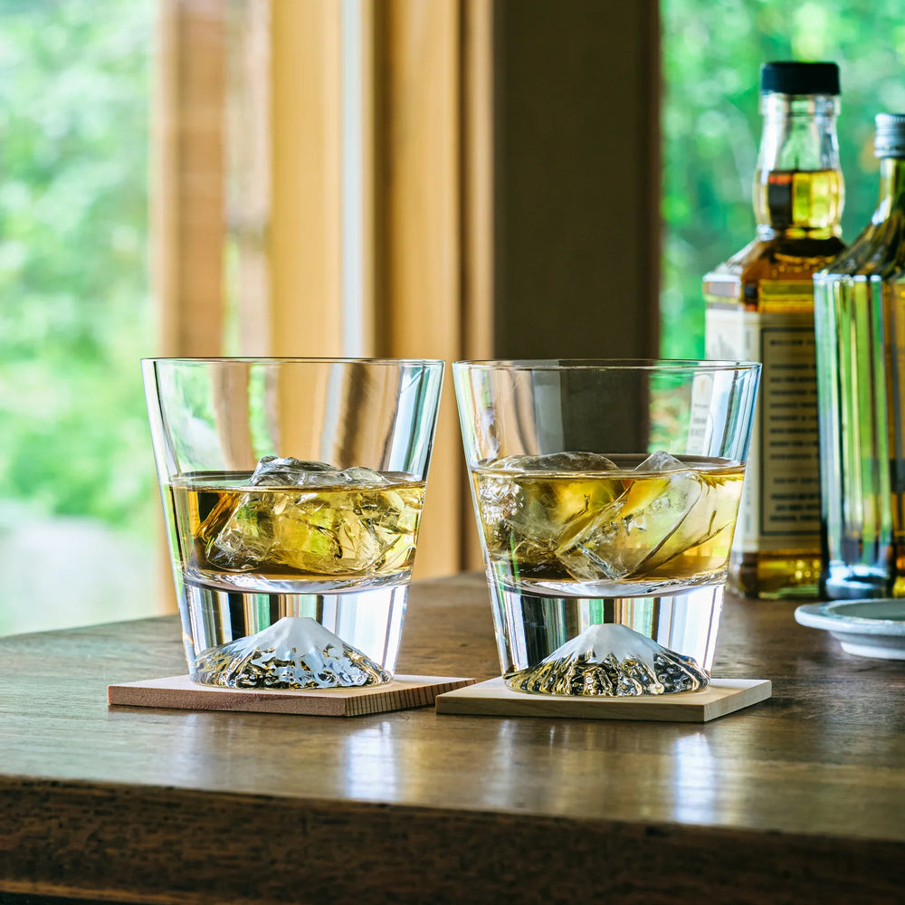 Japanese whiskey glasses with Mt. Fuji design, filled with whiskey and ice, placed on wooden coasters.