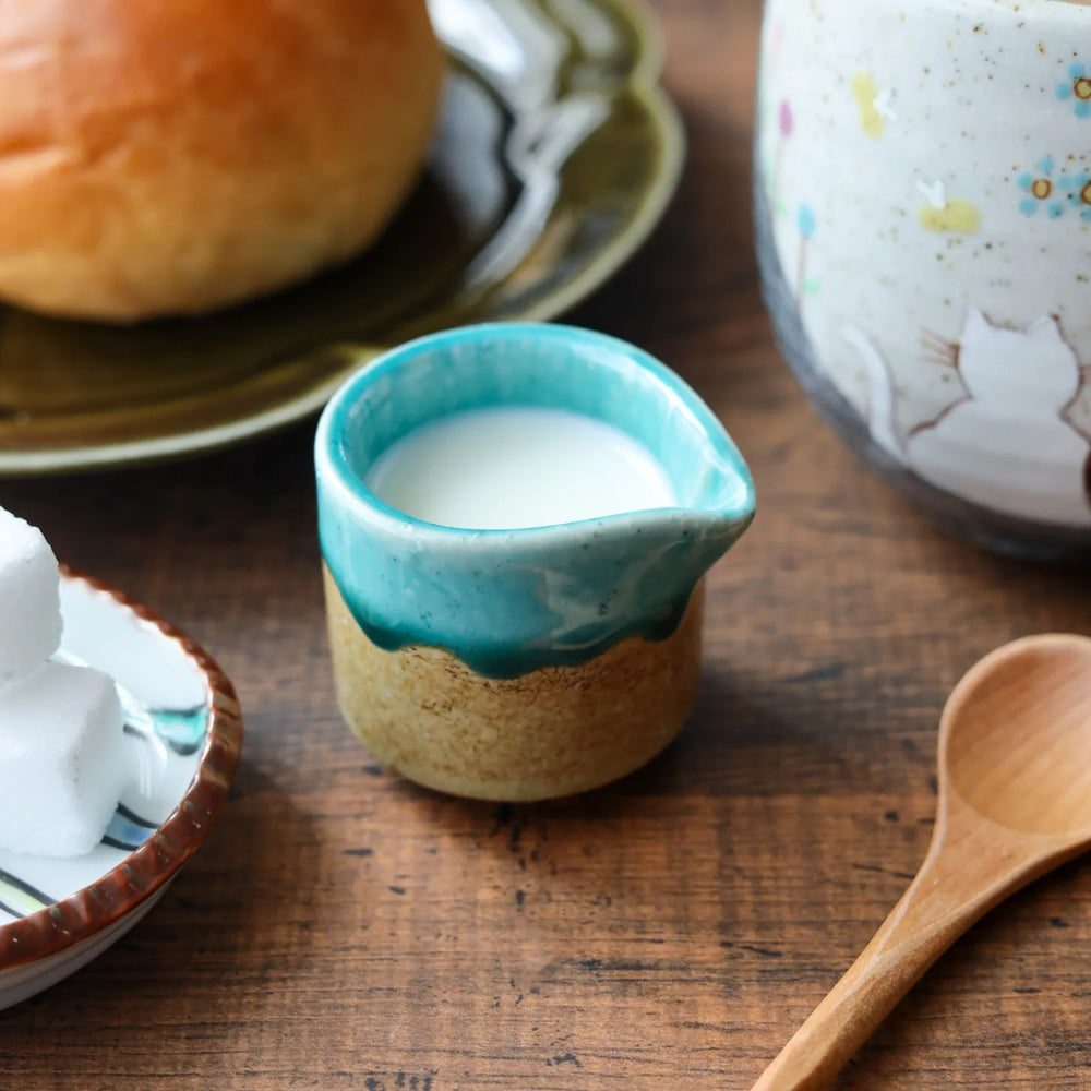 Turquoise and beige ceramic sauce pourer filled with milk, featuring a wave-like rim and compact size perfect for cream or dressings.