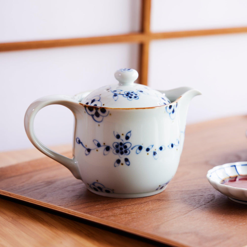Japanese porcelain teapot with blue floral patterns, placed on a wooden tray in a traditional dining setting.