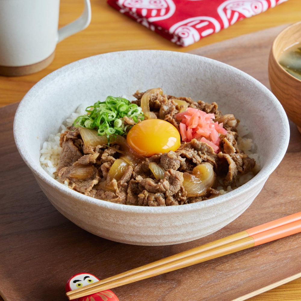 A rustic White Dew Donburi Bowl filled with gyudon—simmered beef, onion, raw egg yolk, and rice—served with miso soup and chopsticks.