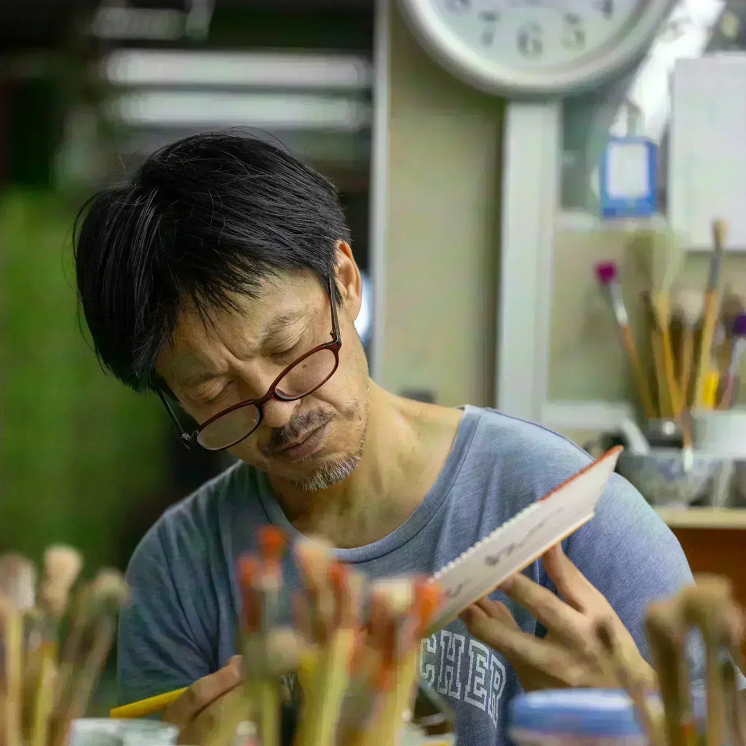 Japanese artisan hand painting porcelain tableware with fine brushwork in a traditional workshop