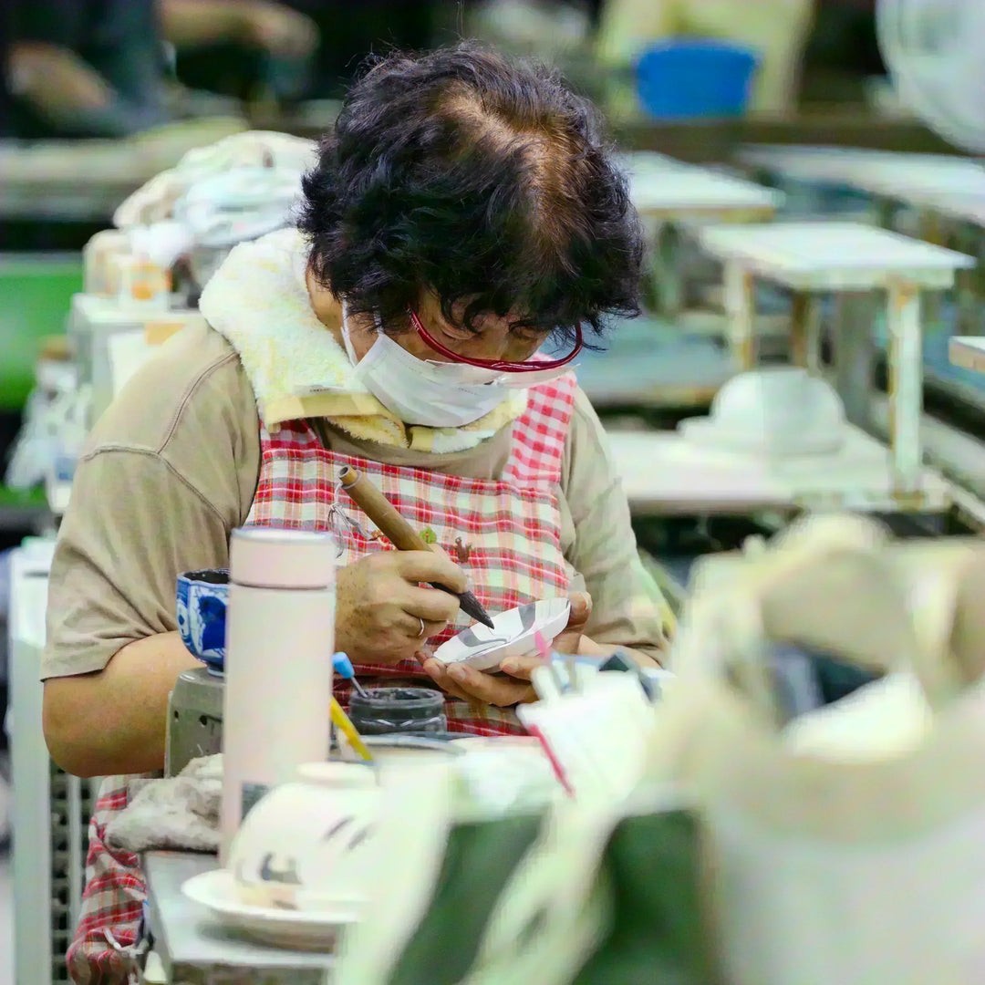 Japanese artisan carefully decorating a small porcelain bowl with detailed brushwork in the studio