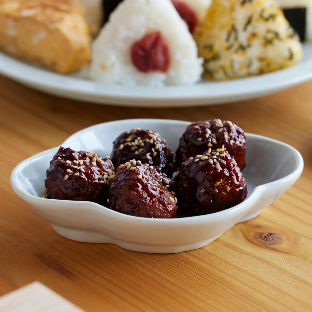Japanese tsukune style meatballs coated in sweet soy glaze and sprinkled with sesame seeds served in a ceramic dish with onigiri