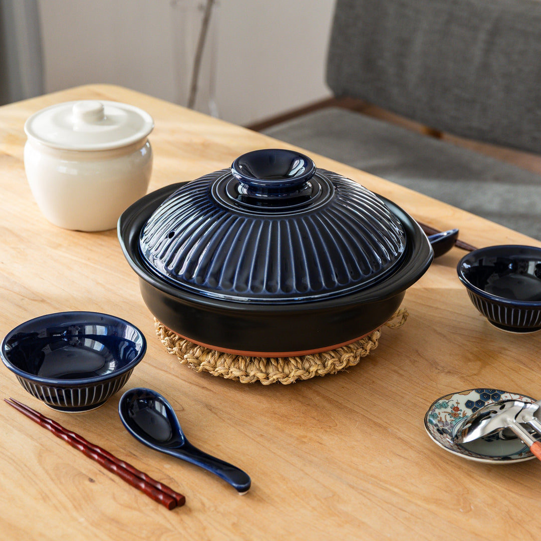 Large artisan straw trivet supporting Japanese donabe on wooden table