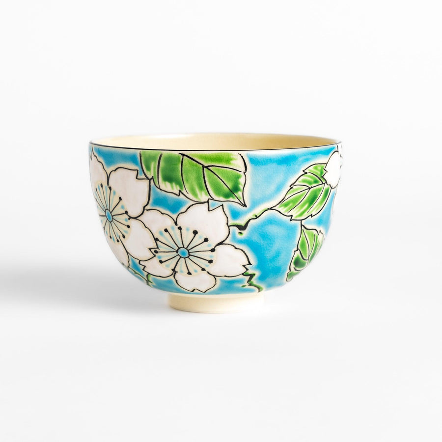 Eye-catching Matcha bowl showcasing a beautiful floral pattern in white and green against a bright blue backdrop, ideal for preparing and serving Matcha.