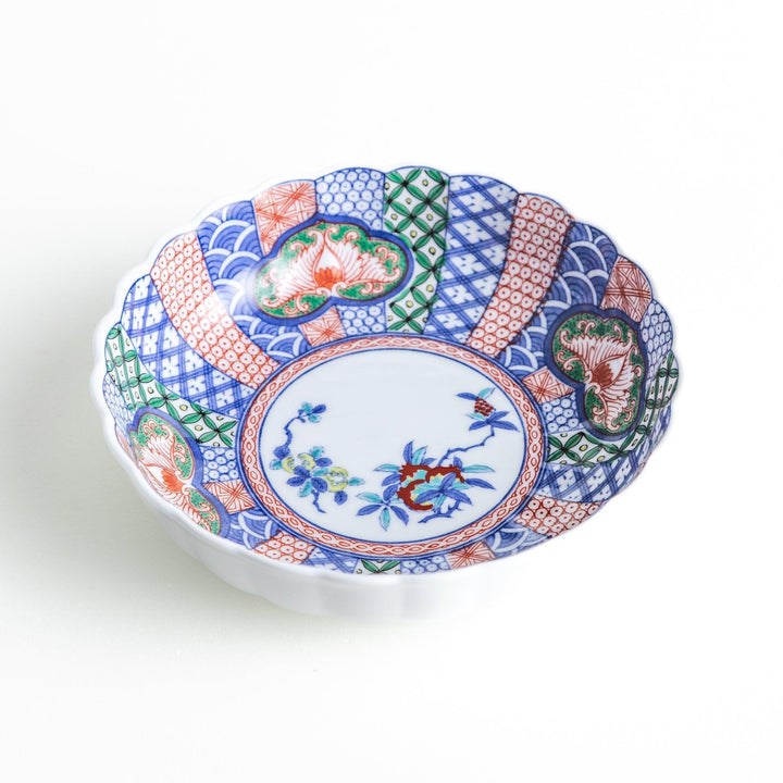 A round, deep cereal bowl with a scalloped edge, featuring a central floral design surrounded by a colorful pattern in blue, red, and green on a white background.