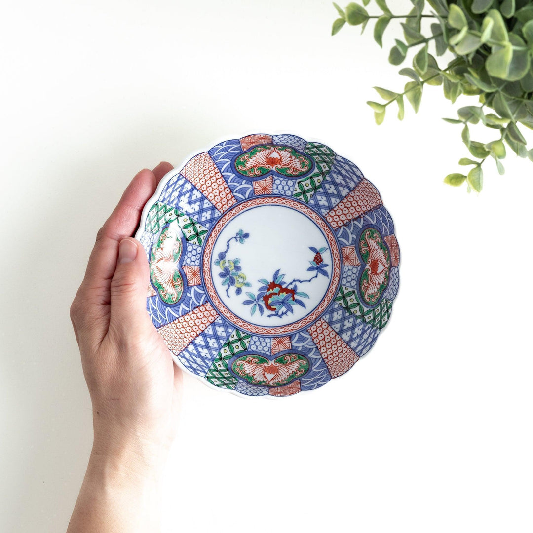 A round, deep cereal bowl with a scalloped edge, featuring a central floral design surrounded by a colorful pattern in blue, red, and green on a white background.