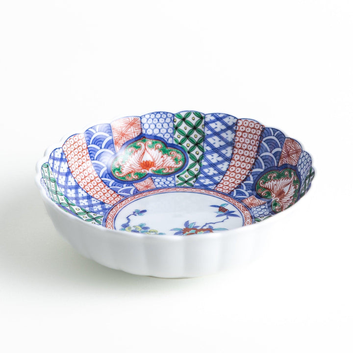 A round, deep cereal bowl with a scalloped edge, featuring a central floral design surrounded by a colorful pattern in blue, red, and green on a white background.