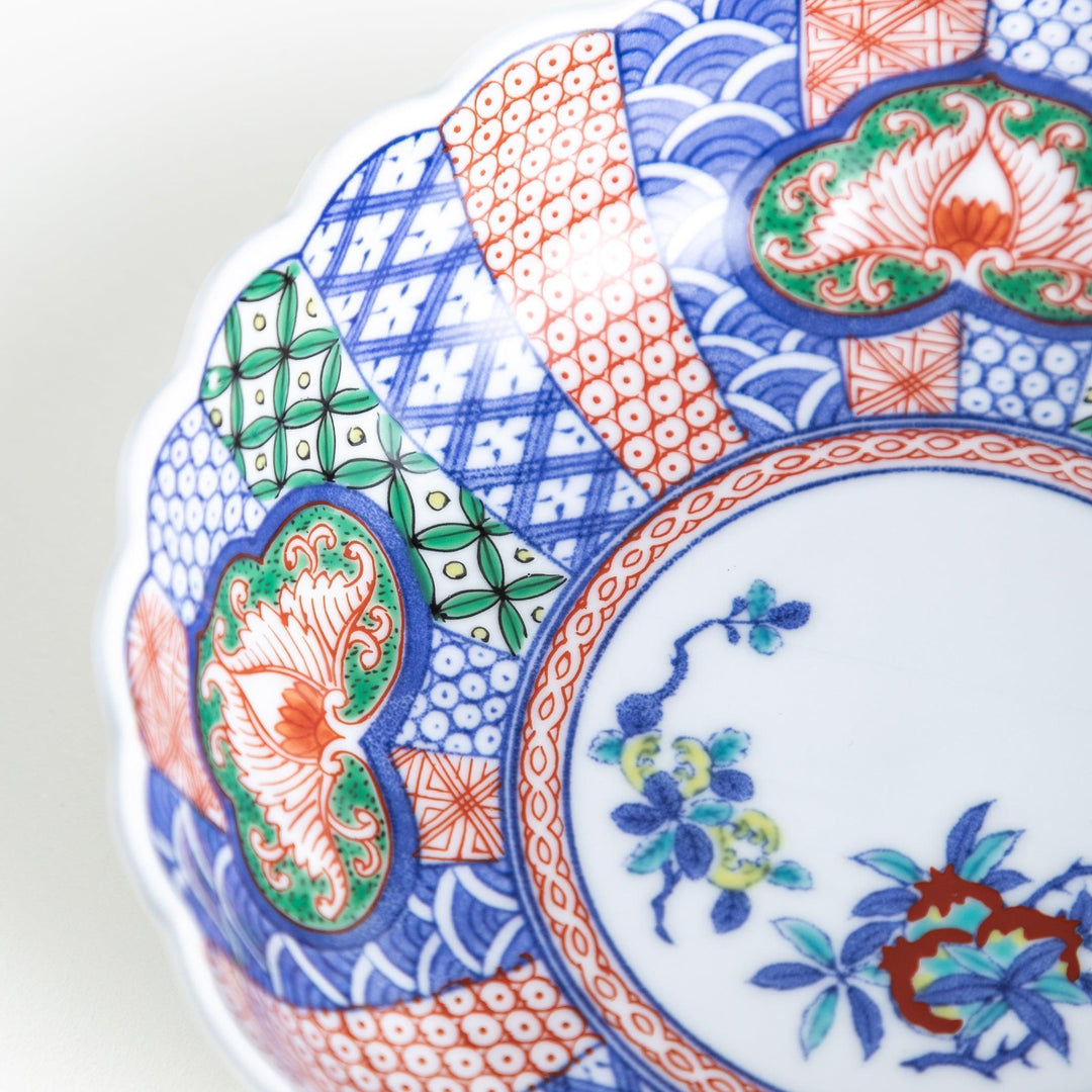 A round, deep cereal bowl with a scalloped edge, featuring a central floral design surrounded by a colorful pattern in blue, red, and green on a white background.