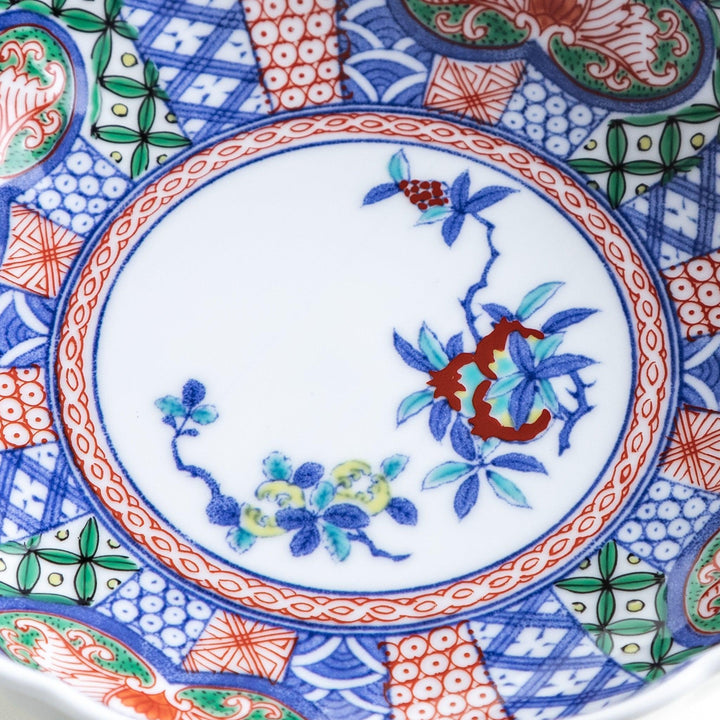 A round, deep cereal bowl with a scalloped edge, featuring a central floral design surrounded by a colorful pattern in blue, red, and green on a white background.