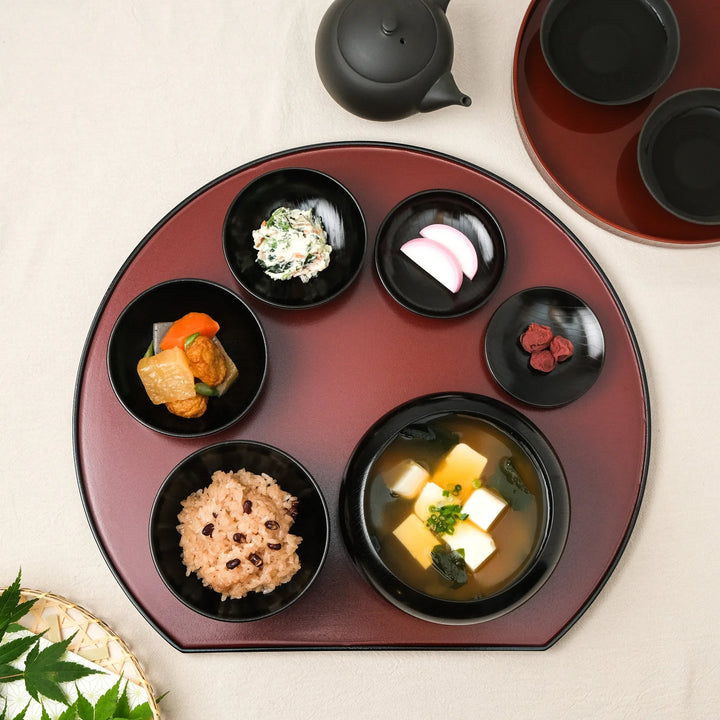 Japanese black lacquered oryoki bowl set with rice, miso soup, and side dishes neatly arranged on a red serving tray