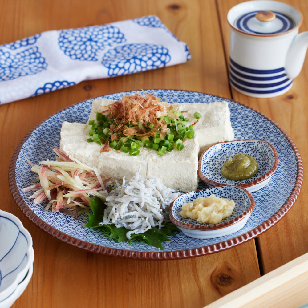 Traditional Japanese cold tofu dish served on a blue patterned plate with grated ginger, myoga, shirasu, and condiments showcasing authentic home dining style.
