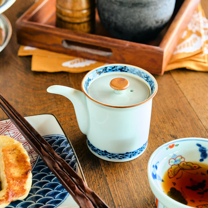 Elegant white soy sauce dispenser with blue floral rim, and fine detailing near the base, placed on a wooden table beside chopsticks.