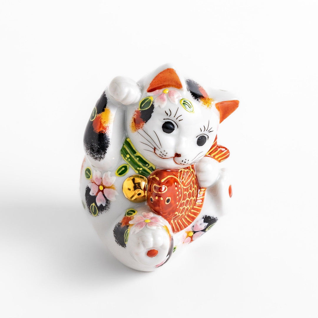 Colorful Calico Maneki Neko figurine holding a lucky sea bream, adorned with floral and green leaf patterns, symbolizing good fortune and prosperity in Japanese culture.