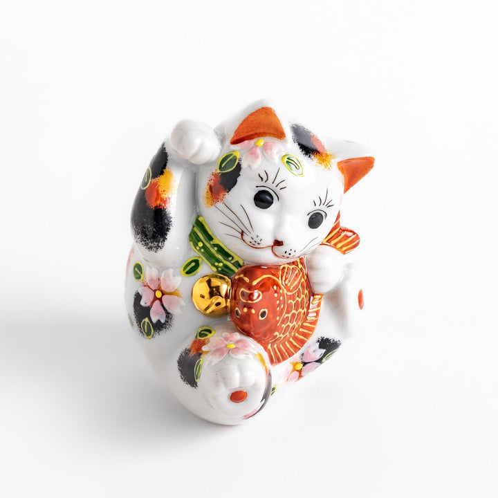 Colorful Calico Maneki Neko figurine holding a lucky sea bream, adorned with floral and green leaf patterns, symbolizing good fortune and prosperity in Japanese culture.