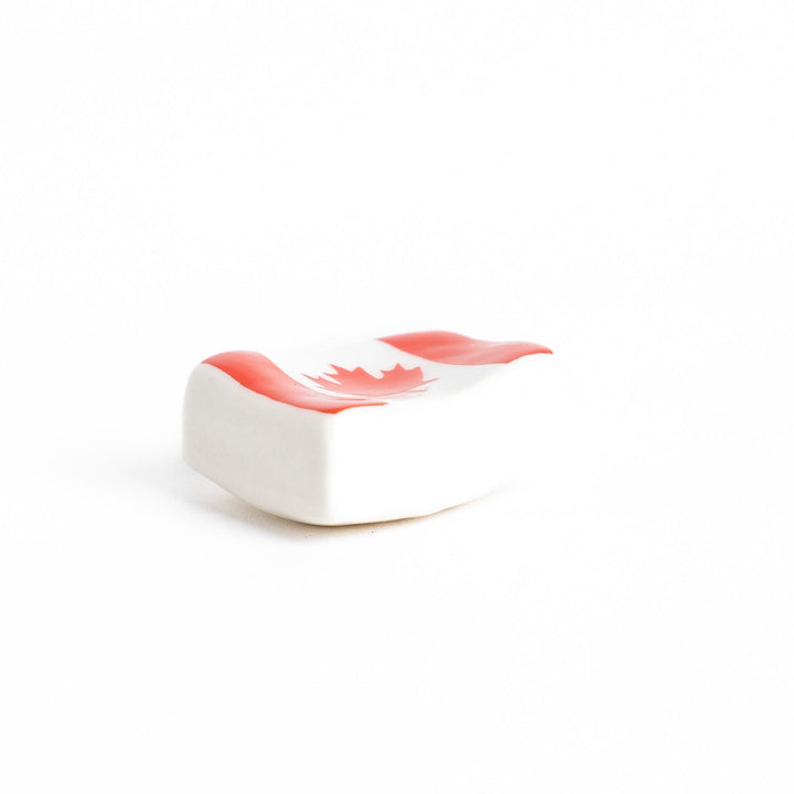 Chopstick rest shaped like the Canadian flag, featuring a red maple leaf in the center, with red borders on each side.