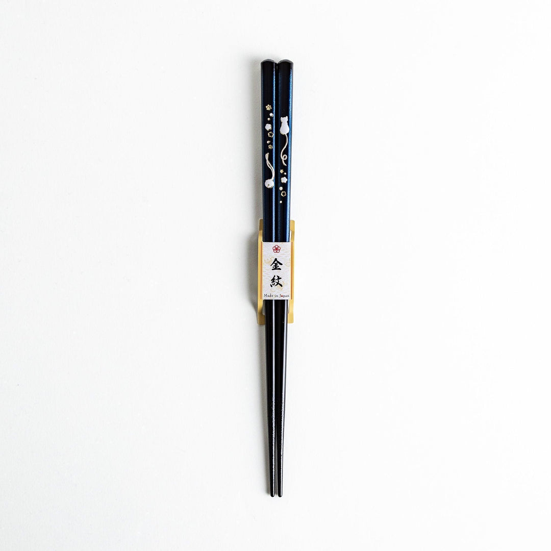 A pair of chopsticks, one blue and one red, each featuring a delicate white cat design near the top.