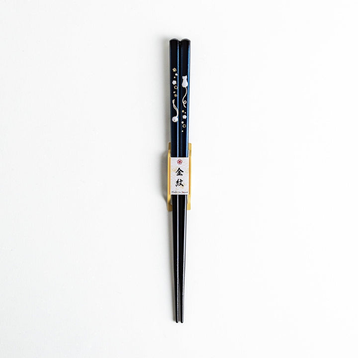 A pair of chopsticks, one blue and one red, each featuring a delicate white cat design near the top.
