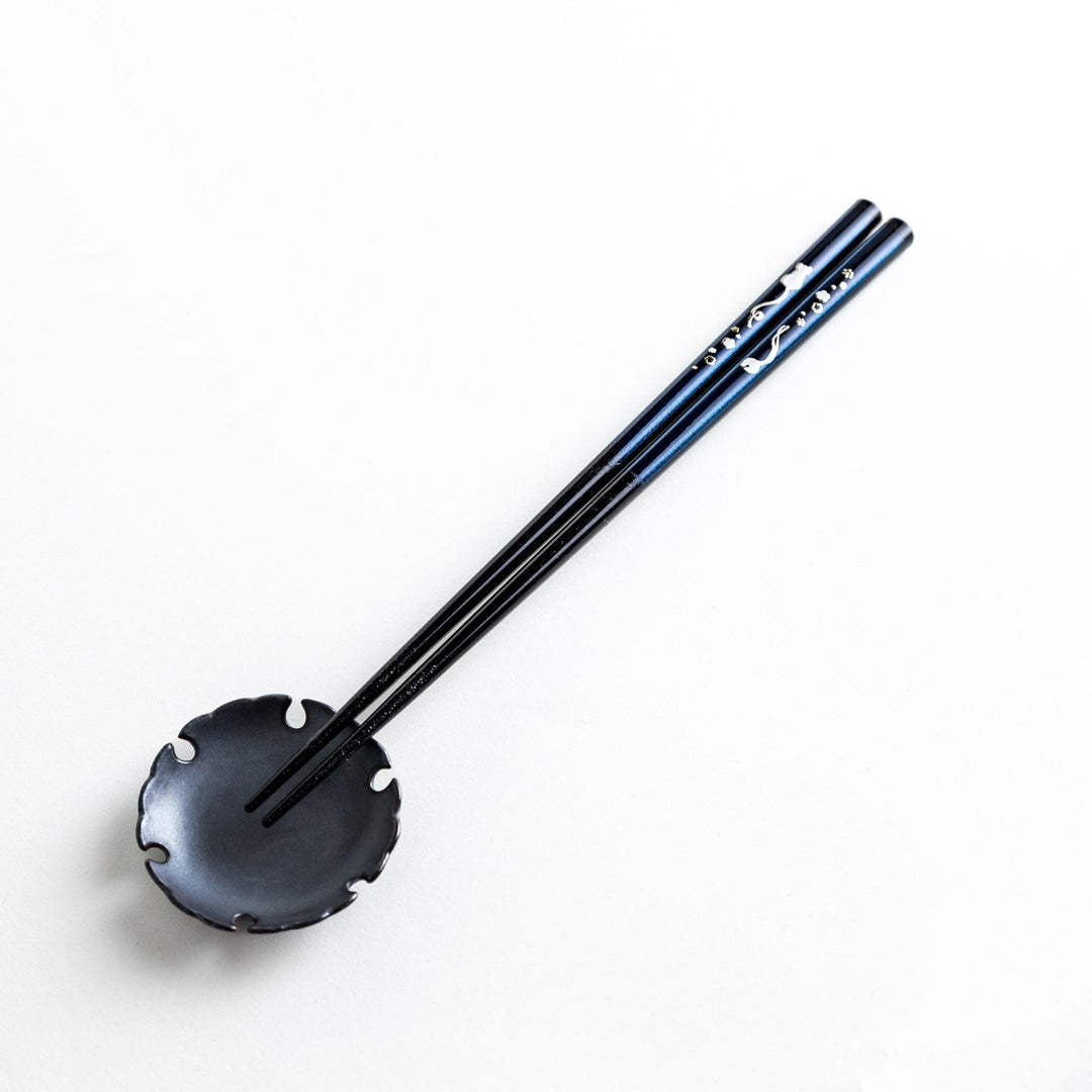 A pair of chopsticks, one blue and one red, each featuring a delicate white cat design near the top.