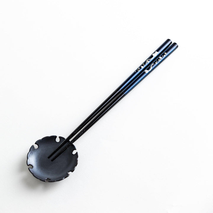 A pair of chopsticks, one blue and one red, each featuring a delicate white cat design near the top.