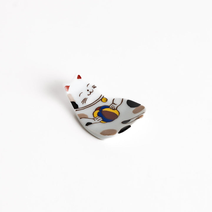 Ceramic chopsticks rest shaped like a cat holding a ball, featuring detailed brown, black, and red accents with a charming expression.