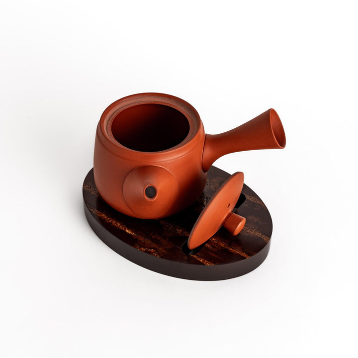 Red clay teapot with lid resting on an oval-shaped cherry bark teapot rest, adding a touch of traditional Japanese elegance to your tea service.