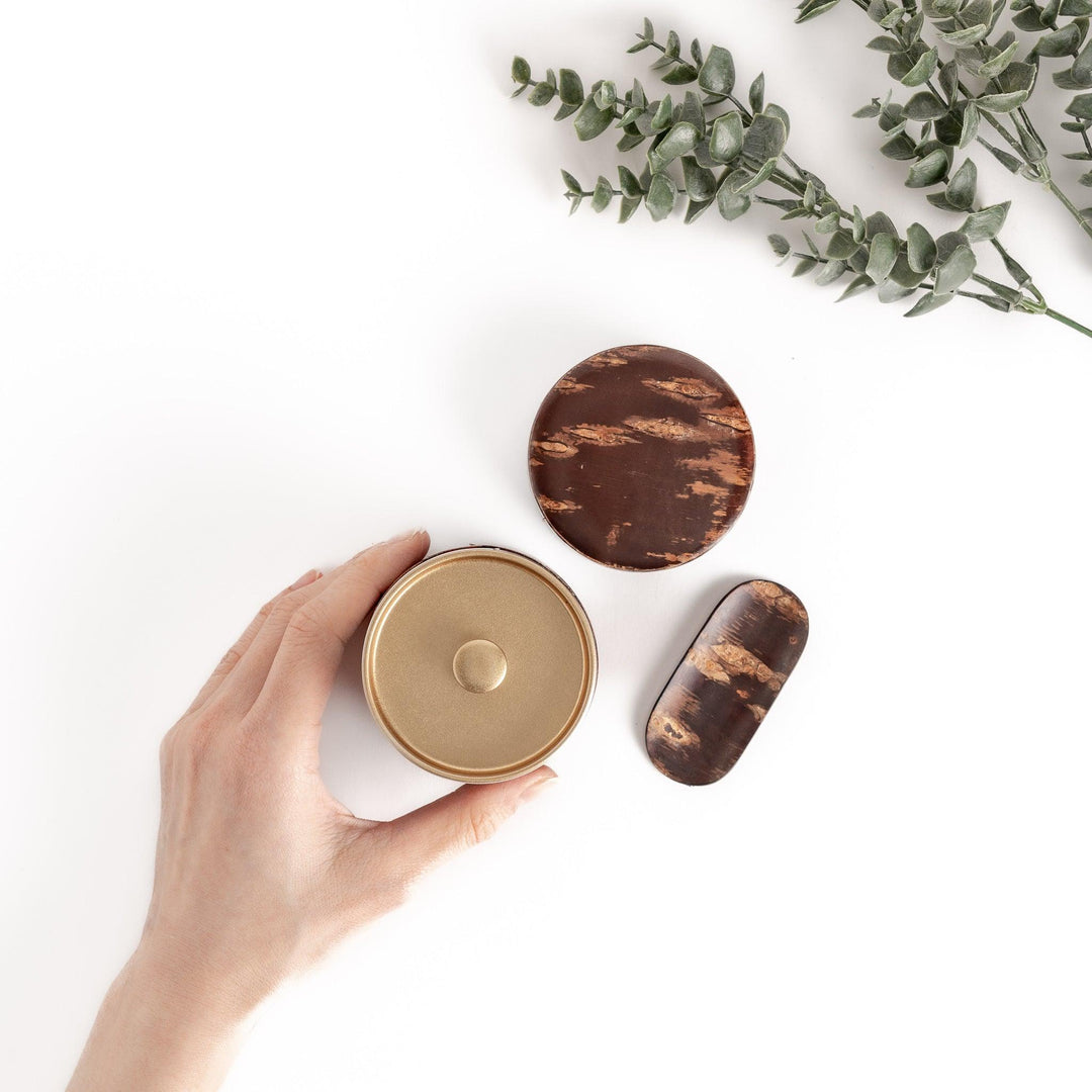 Hand presenting a cherry bark tea caddy and scoop set with a unique grain pattern, perfect for storing and serving loose leaf tea with a touch of rustic elegance.