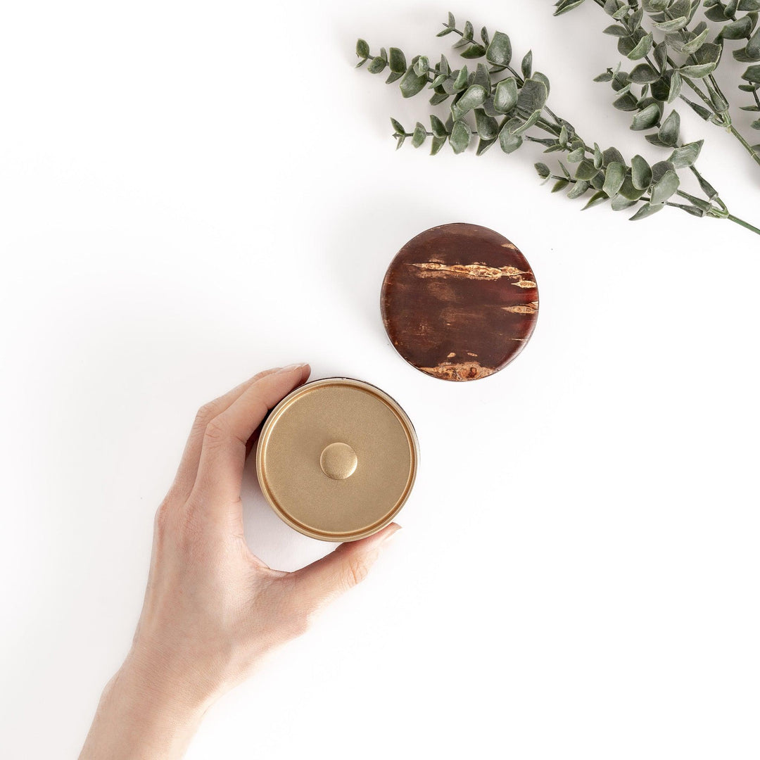 Hand holding a cherry bark tea canister with a separate lid, showcasing the beautiful wood grain and a golden interior, ideal for keeping tea fresh.