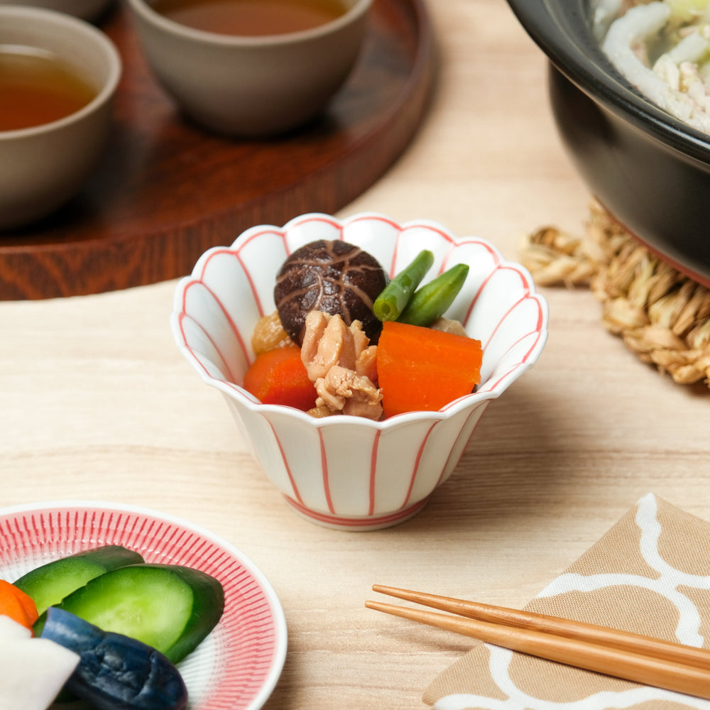 White scalloped Japanese bowl with red vertical lines, filled with simmered vegetables including carrot, shiitake mushroom, green beans, and chicken for a traditional side dish.