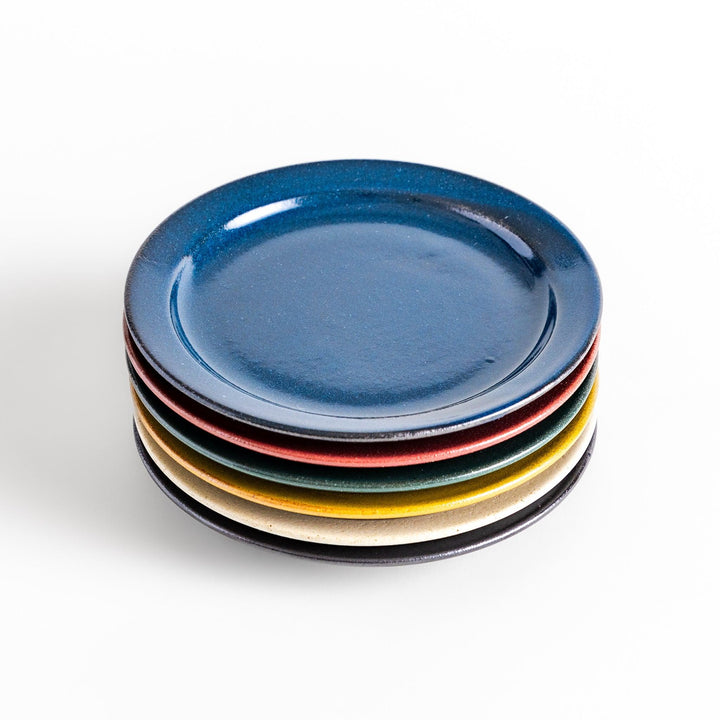 A stack of six colorful dessert plates in blue, red, green, yellow, white, and black, each with a smooth, glossy finish, perfect for adding a pop of color to your table.
