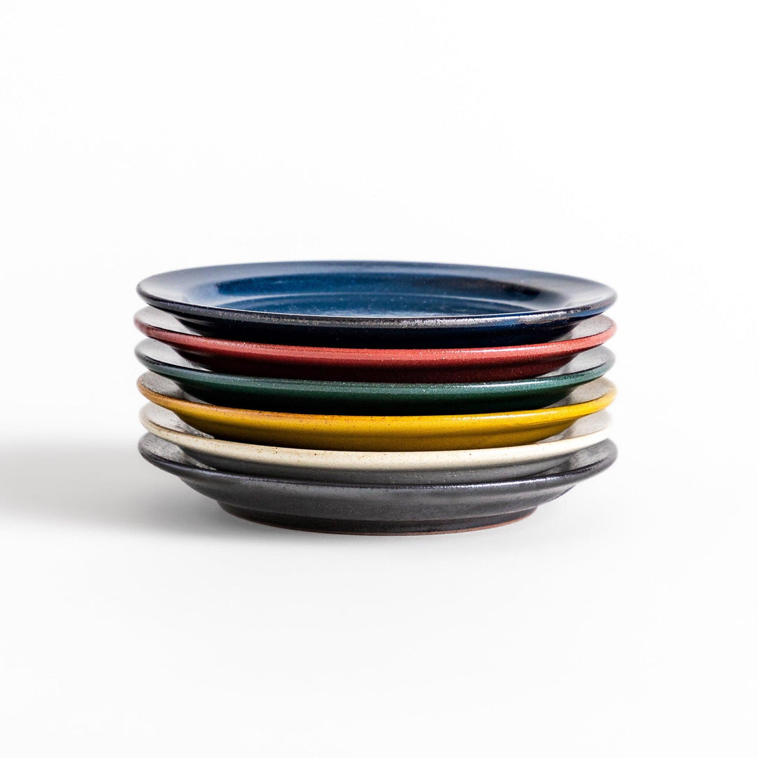 A stack of six colorful dessert plates in blue, red, green, yellow, white, and black, each with a smooth, glossy finish, perfect for adding a pop of color to your table.