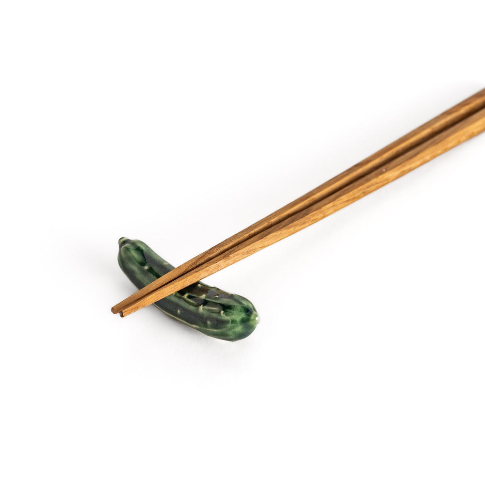 Wooden chopsticks resting on a glossy green ceramic cucumber chopstick rest, showcasing its playful design and functional elegance.