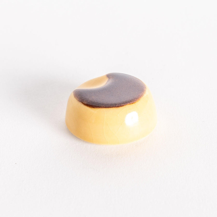 A ceramic chopsticks rest shaped like a custard pudding, featuring a glossy brown caramel top and creamy yellow base.