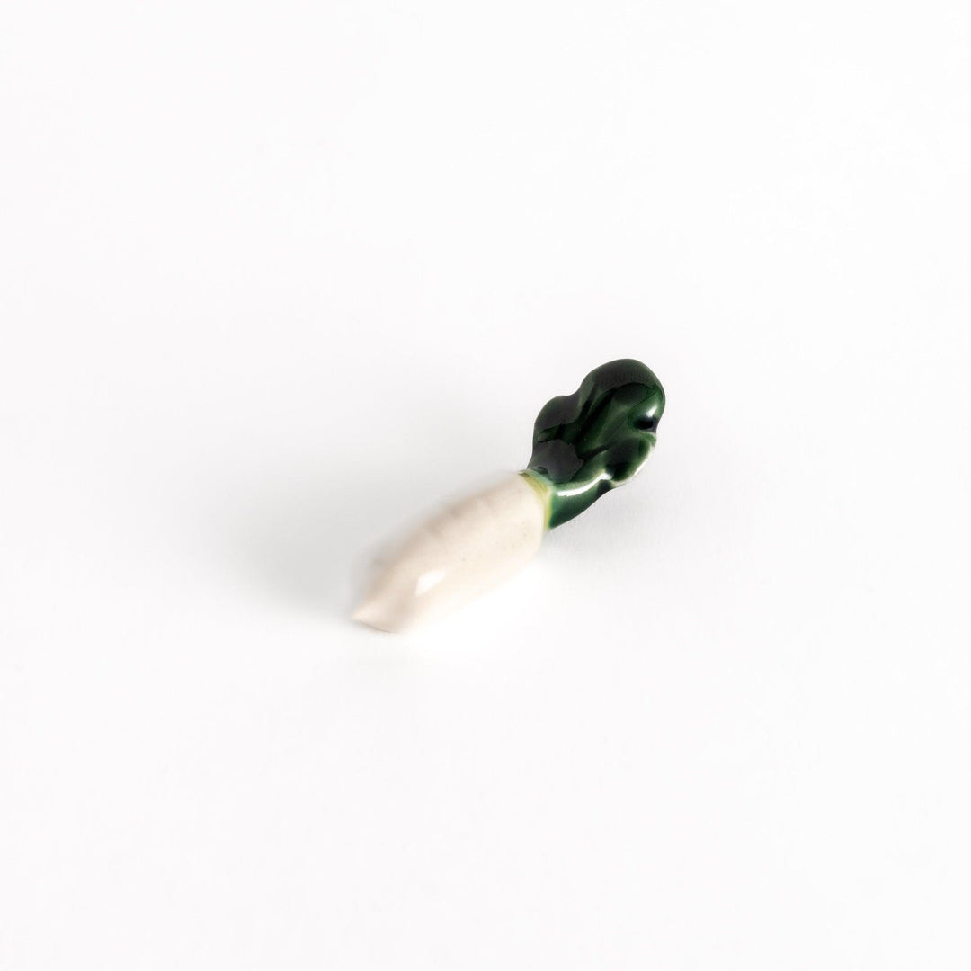 Glossy ceramic chopstick rest shaped like a daikon radish, with a green top and white body, showcasing realistic vegetable details.