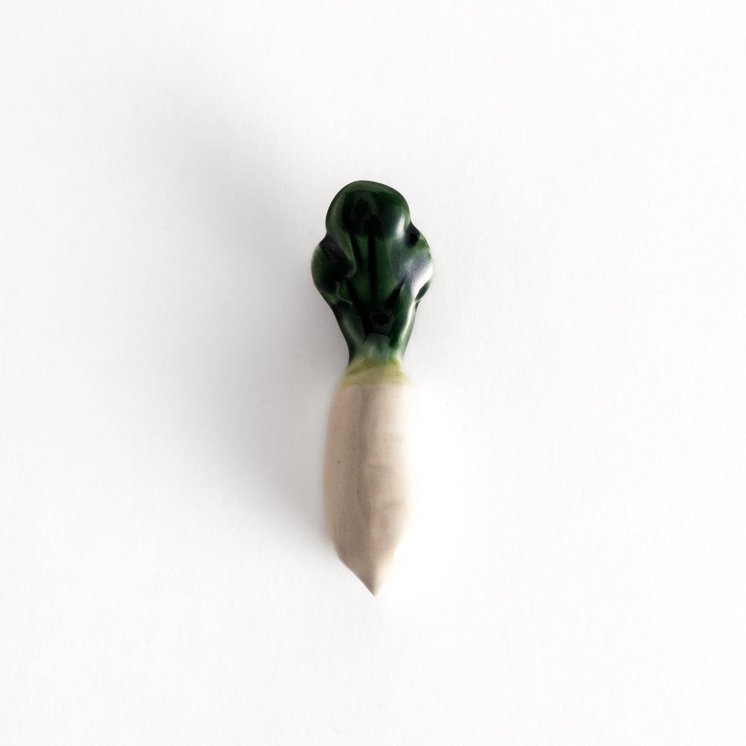 Glossy ceramic chopstick rest shaped like a daikon radish, with a green top and white body, showcasing realistic vegetable details.