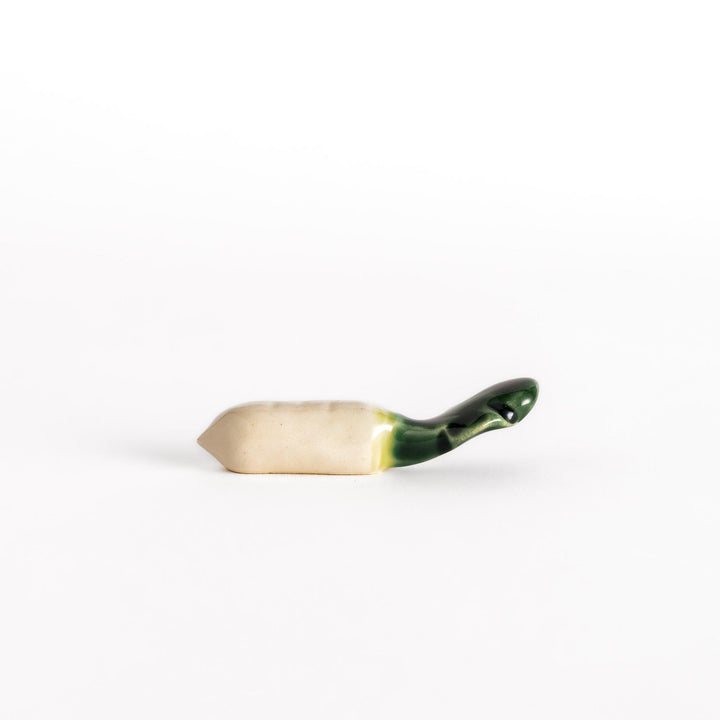 Glossy ceramic chopstick rest shaped like a daikon radish, with a green top and white body, showcasing realistic vegetable details.