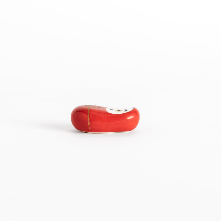 A side view of the red daruma chopstick rest, showcasing its smooth surface and elegant gold cord decoration.