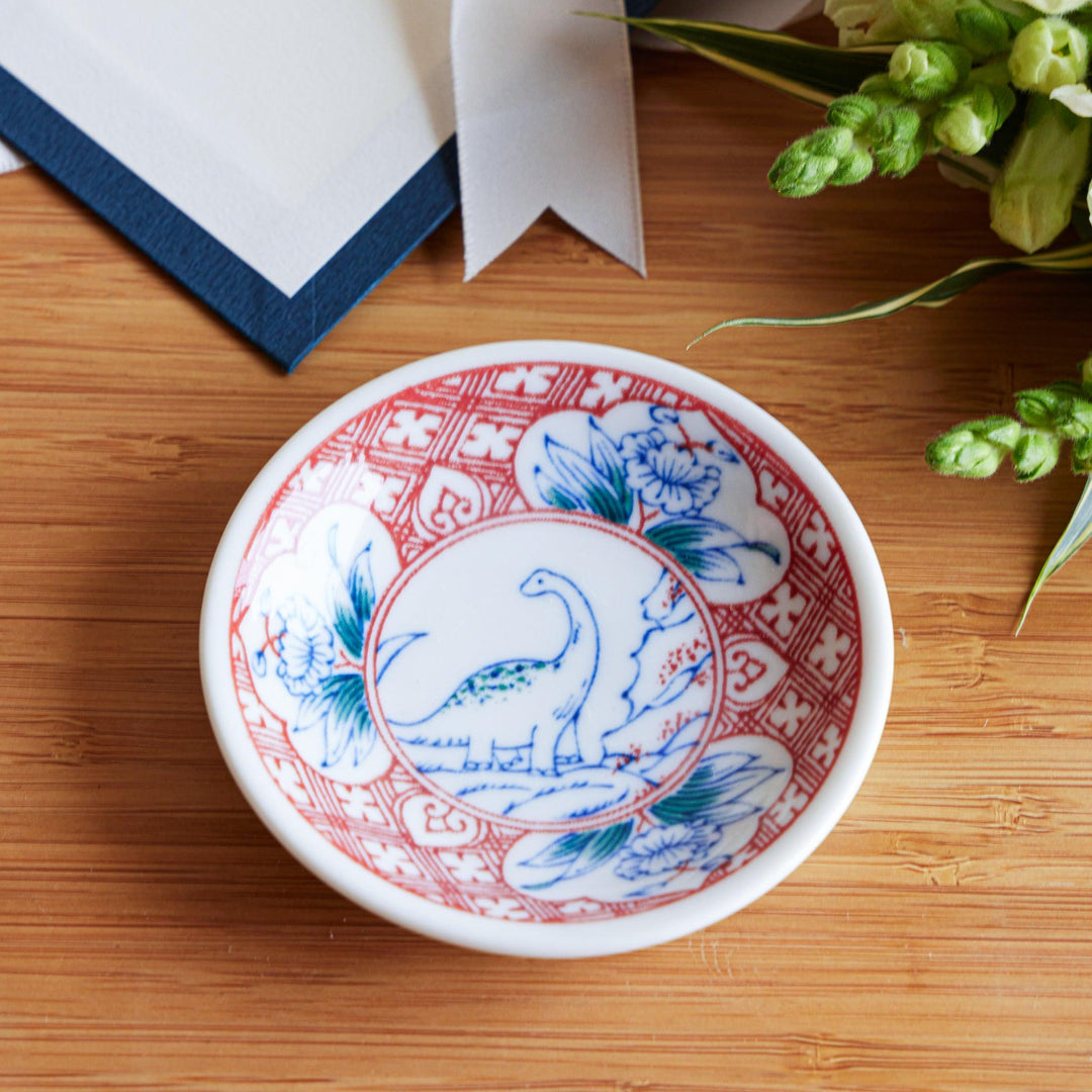 A set of four small, decorative porcelain plates in a gift box, each plate featuring a different dinosaur design in blue and red.