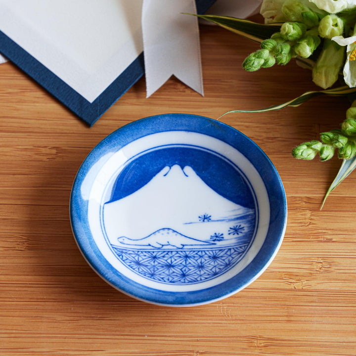 A set of four small, decorative porcelain plates in a gift box, each plate featuring a different dinosaur design in blue and red.