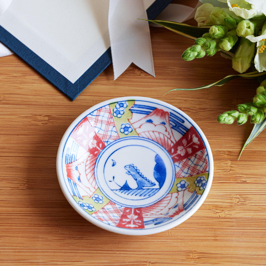 A set of four small, decorative porcelain plates in a gift box, each plate featuring a different dinosaur design in blue and red.